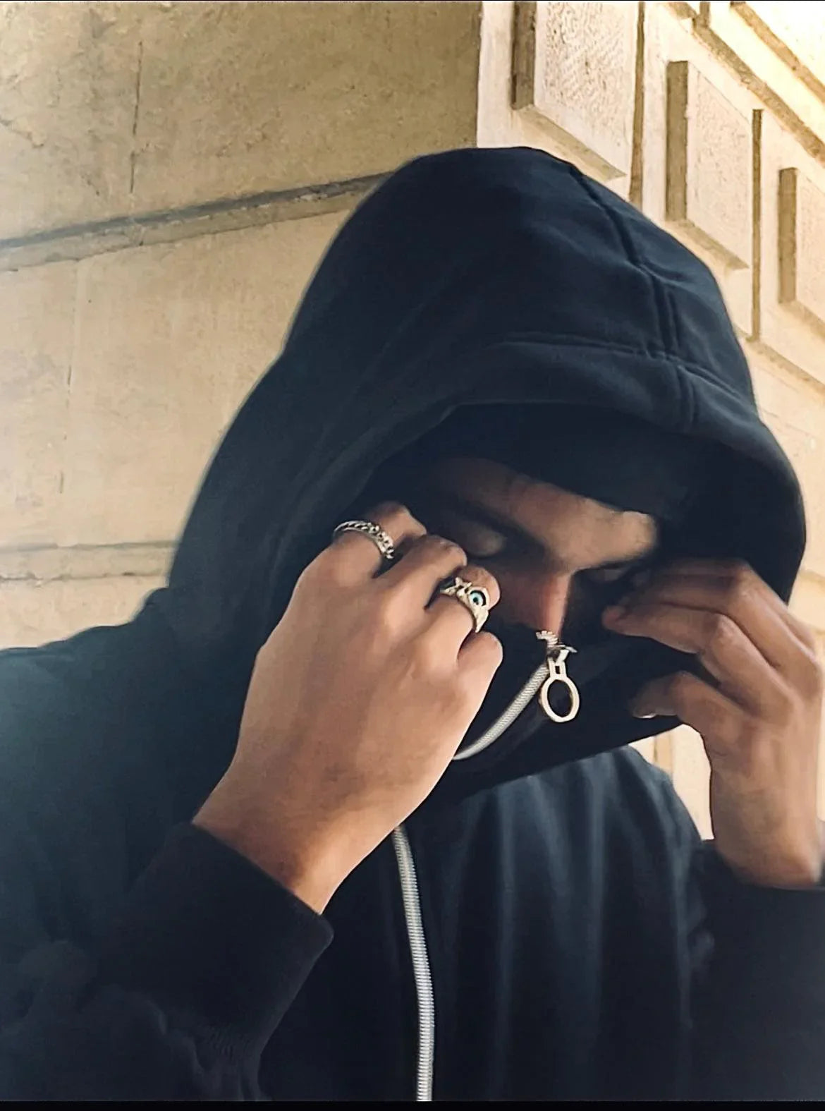 Man in a black zip-up hoodie with silver rings, Y2K streetwear style, urban backdrop