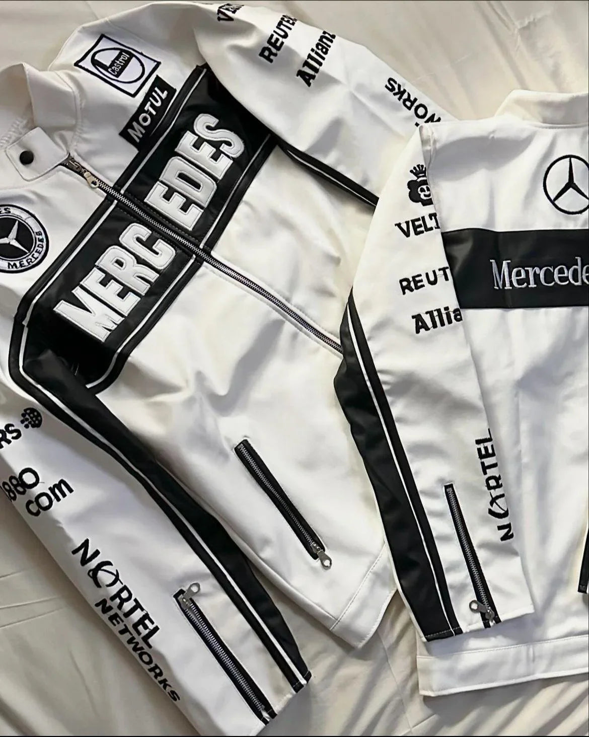 White F1 aesthetic track jackets with black details and sponsor logos, laid flat on fabric.