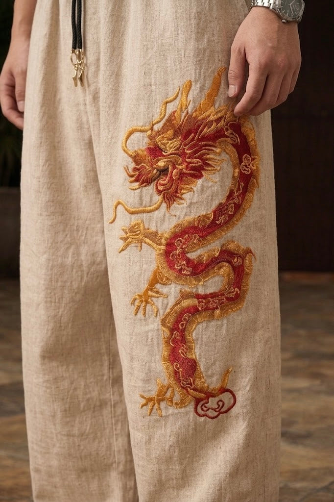 Detail shot of the elasticated drawstring waistband and metal toggles on beige wide-leg Chinese dragon pants styled with a red shirt.