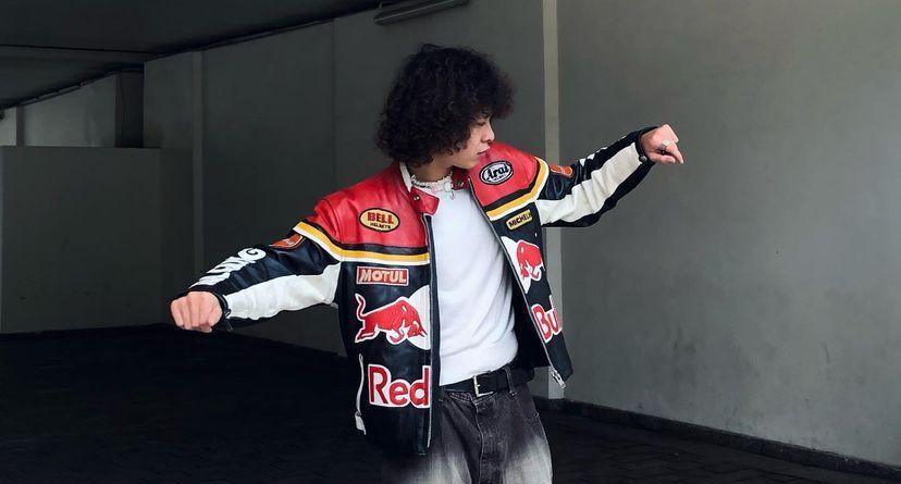Man in navy Red Bull racing leather jacket with boxy streetwear silhouette posing outdoors