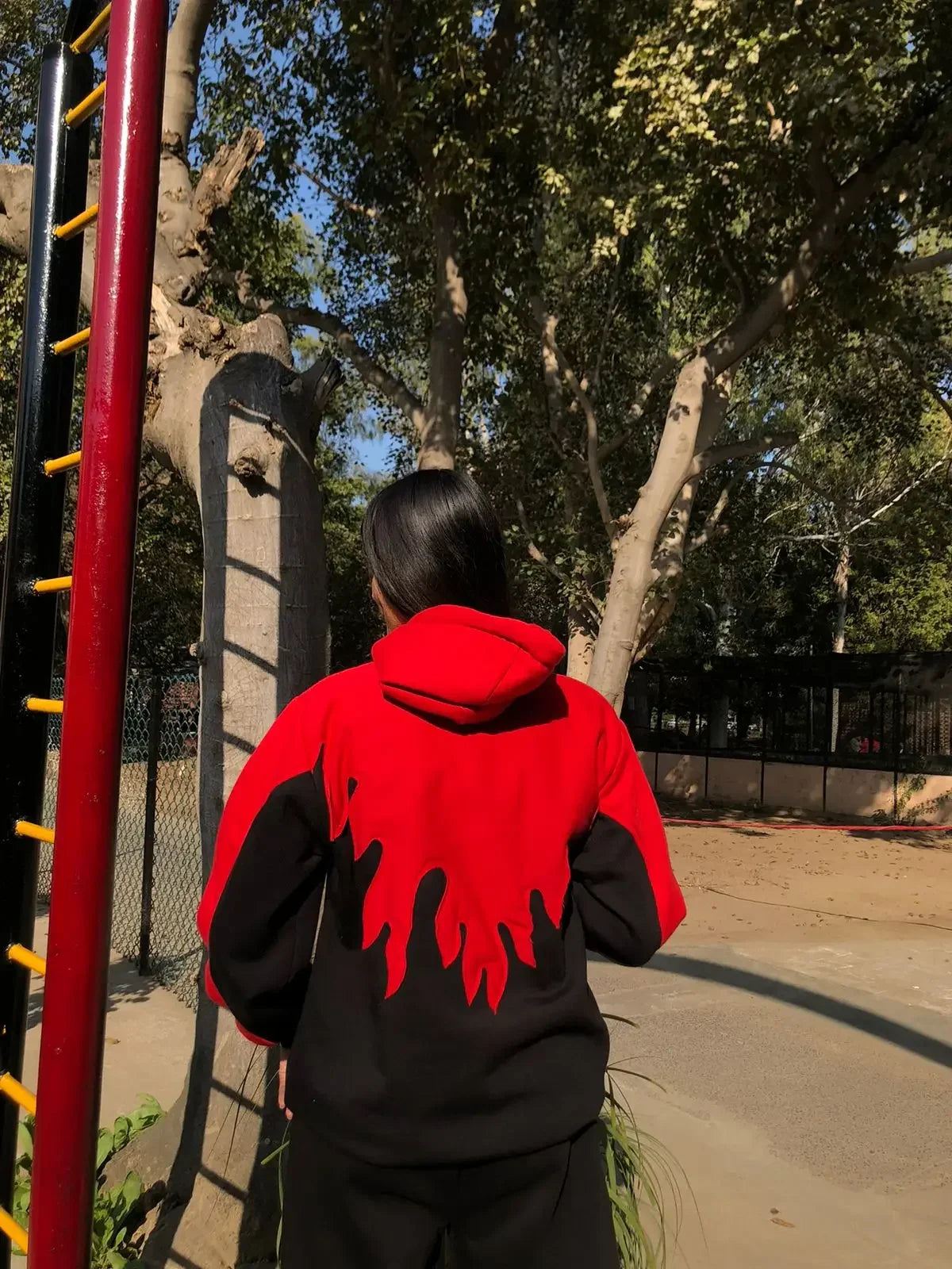Person wearing a red and black streetwear hoodie with flame design on the back outdoors