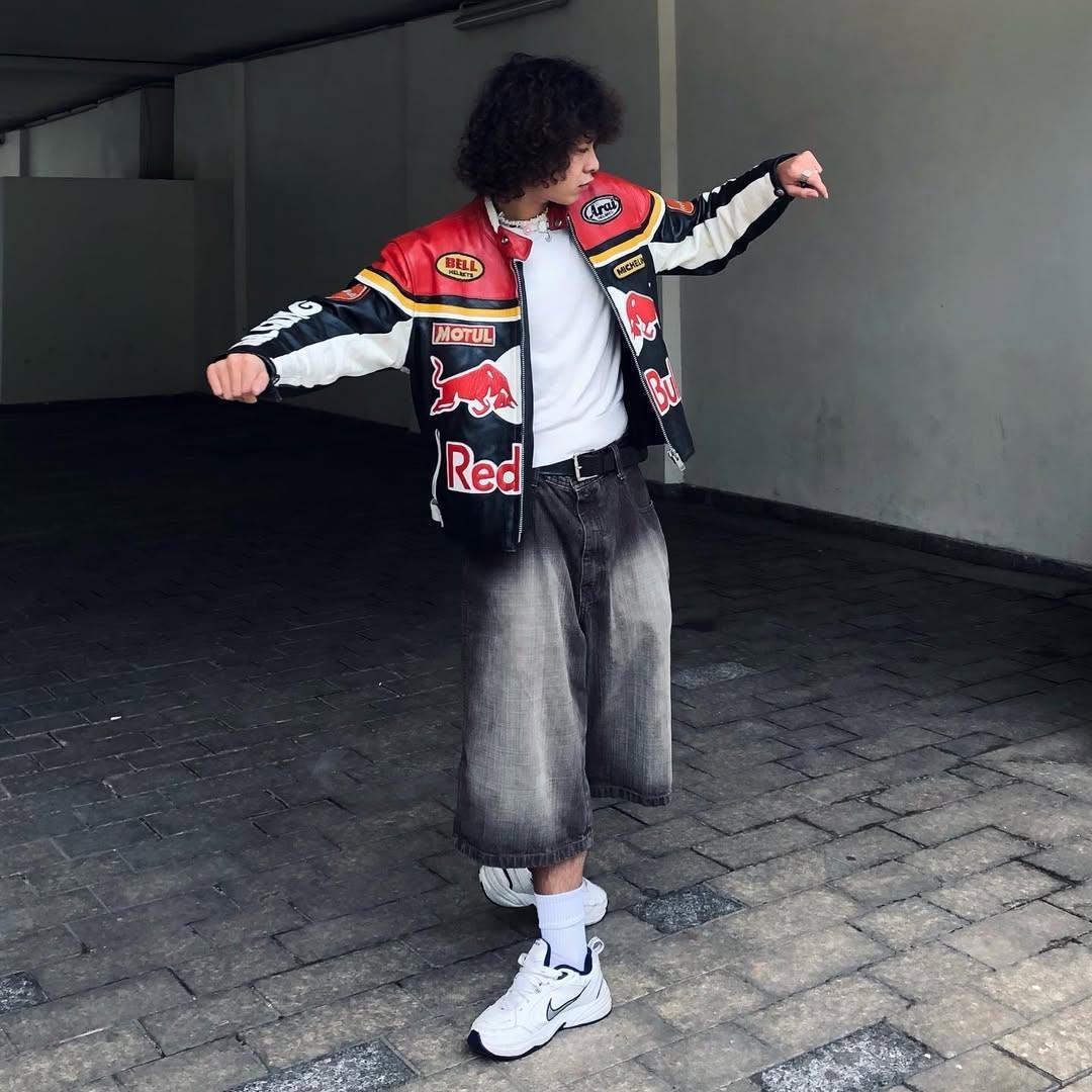 Person wearing a Red Bull F1 motorsport jacket, baggy shorts, and white sneakers in an urban setting.