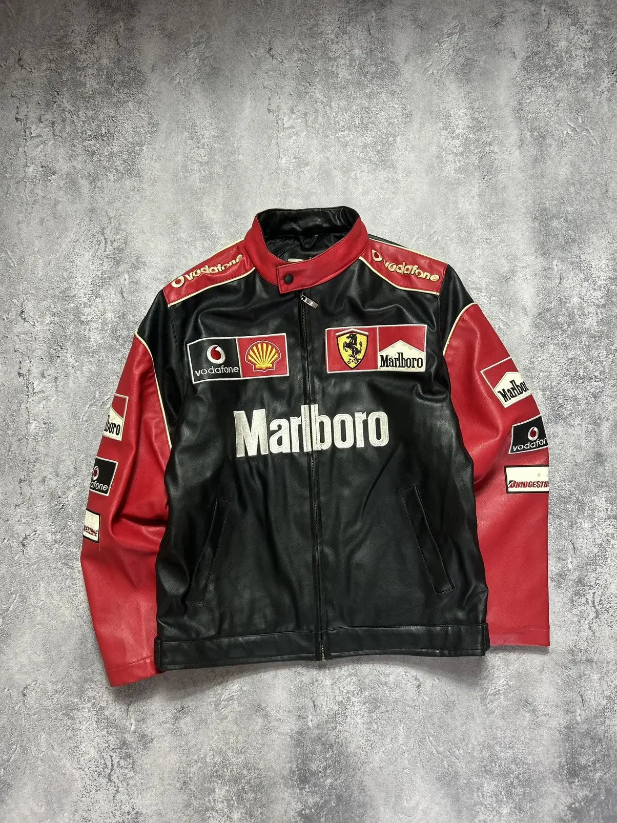 Vintage black and red racing jacket with Ferrari, Shell, and Marlboro logos on grey background.