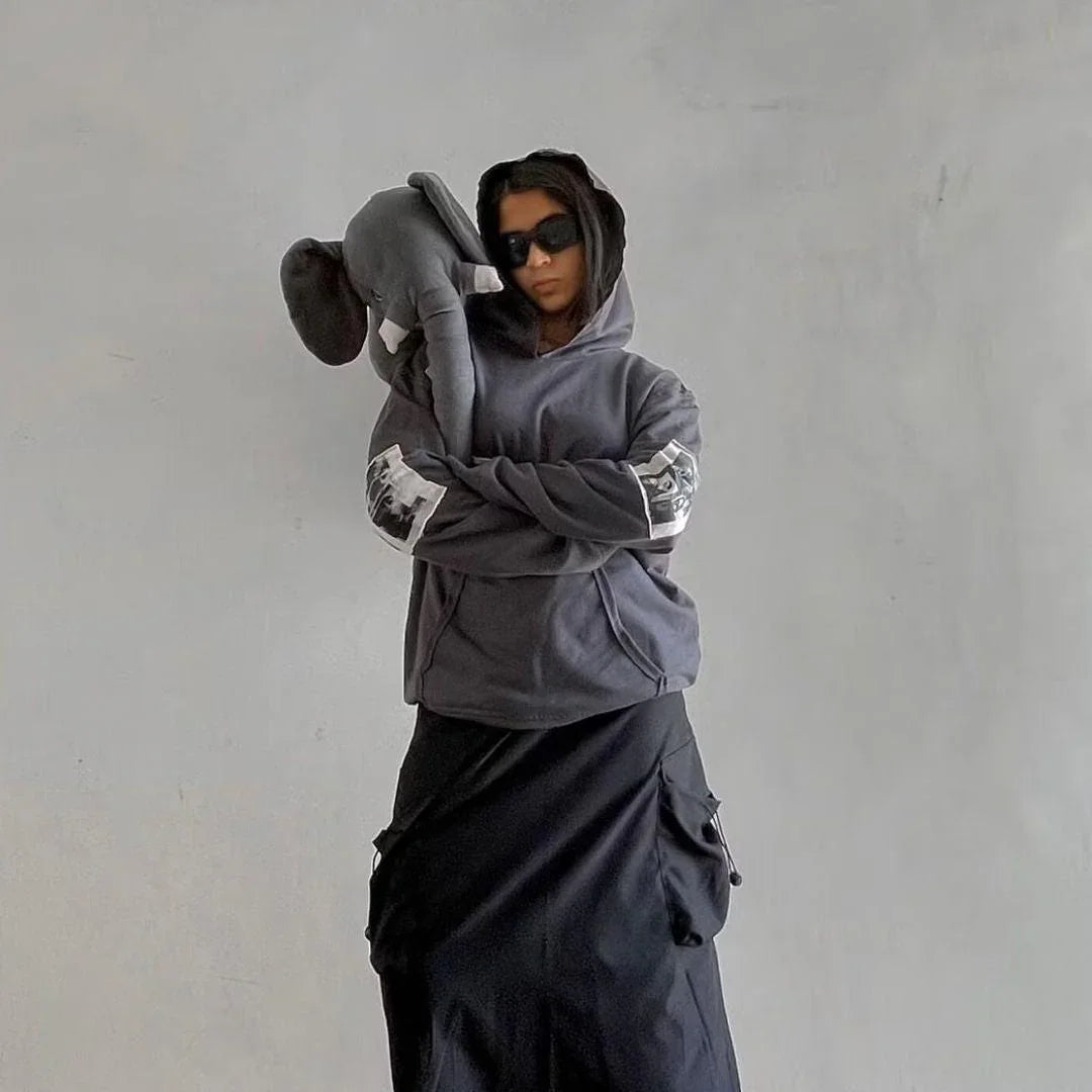 Person in dark streetwear hoodie and black skirt with elephant plush, urban minimalist style