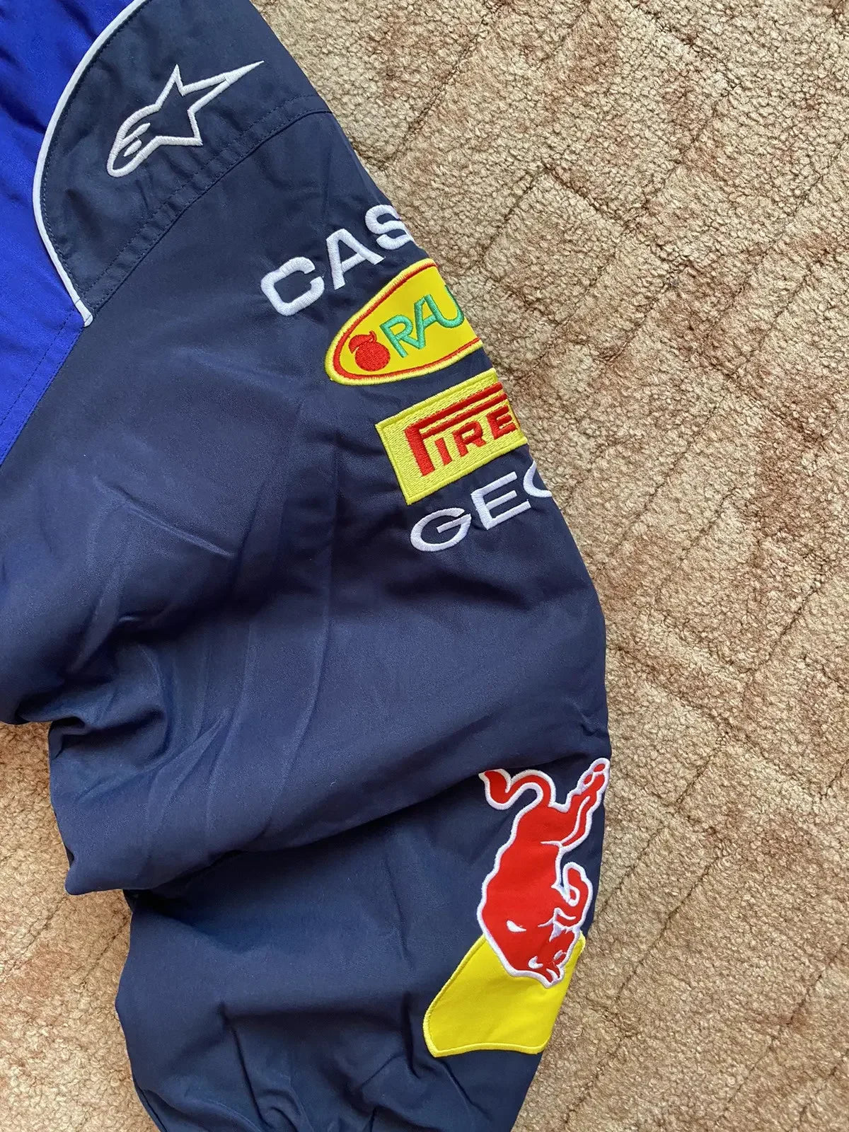 Navy blue F1-inspired streetwear jacket sleeve with embroidered racing patches and logos.